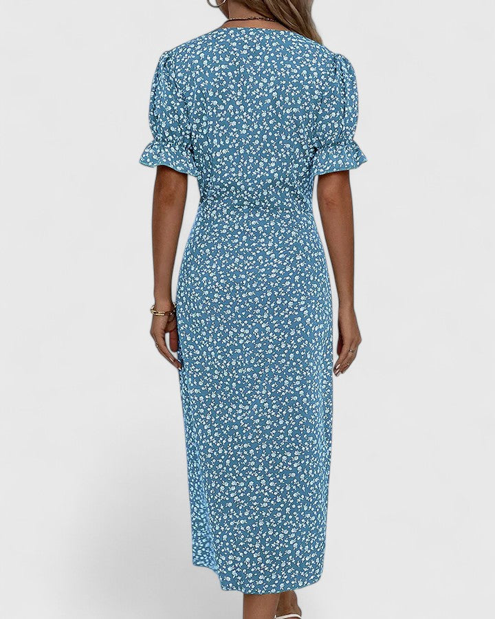 Blue - A woman wearing a green midi dress with a white ditsy floral print, featuring short puff sleeves, a V-neckline, and decorative side buttons with a ruched wrap skirt.