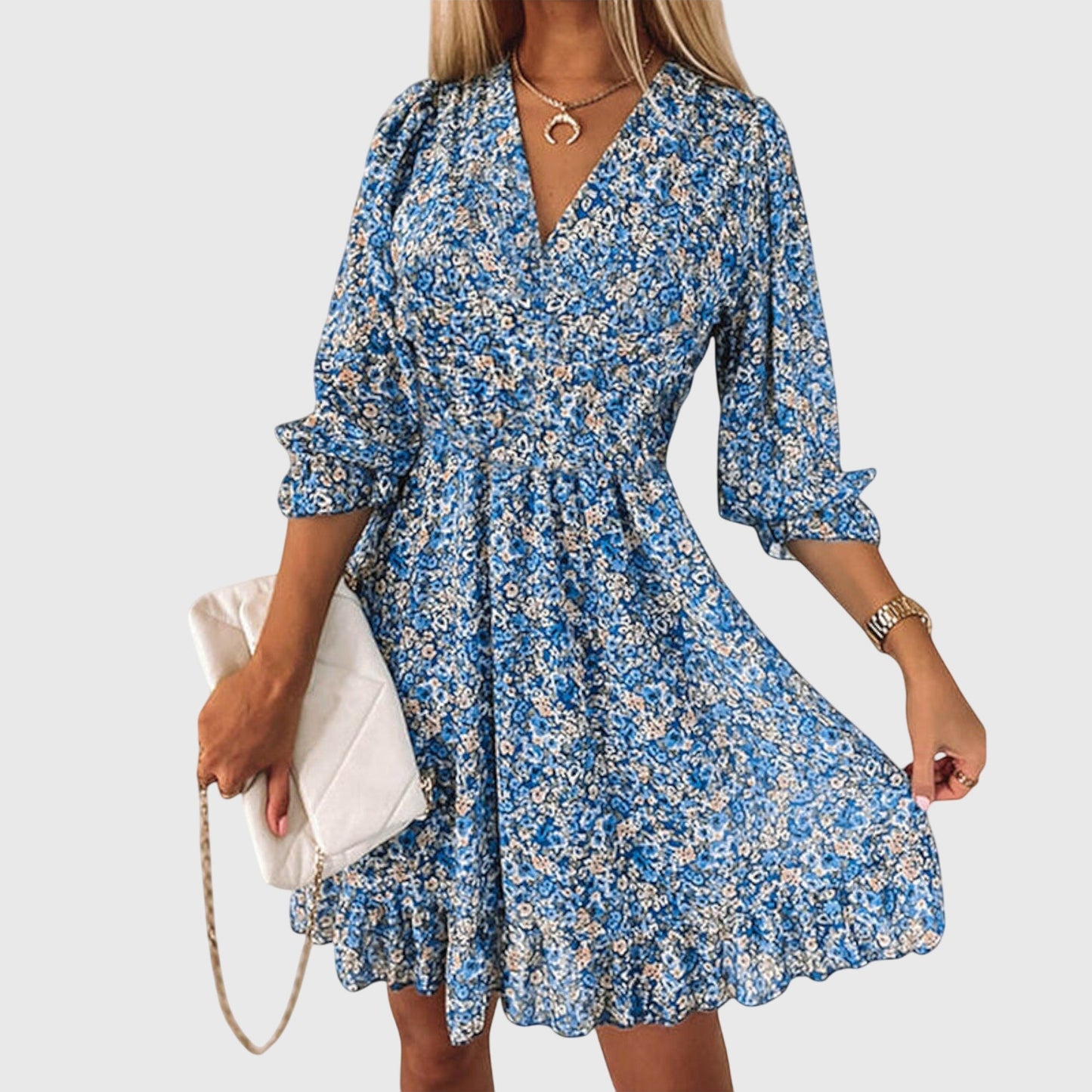 Blue - A woman wearing a blue and white ditsy floral print sundress with a v-neckline, three-quarter sleeves, a cinched waist, and a ruffled hem, holding a white quilted clutch bag.