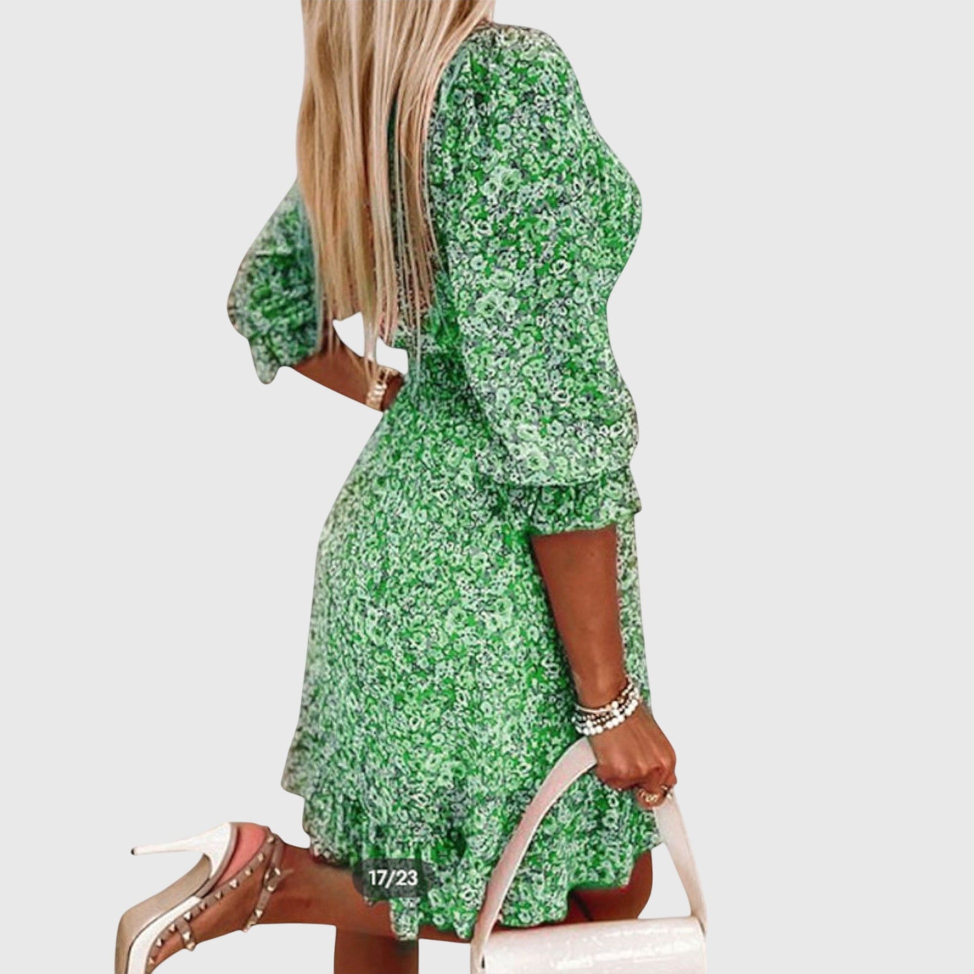Green - A woman wearing a blue and white ditsy floral print sundress with a v-neckline, three-quarter sleeves, a cinched waist, and a ruffled hem, holding a white quilted clutch bag.