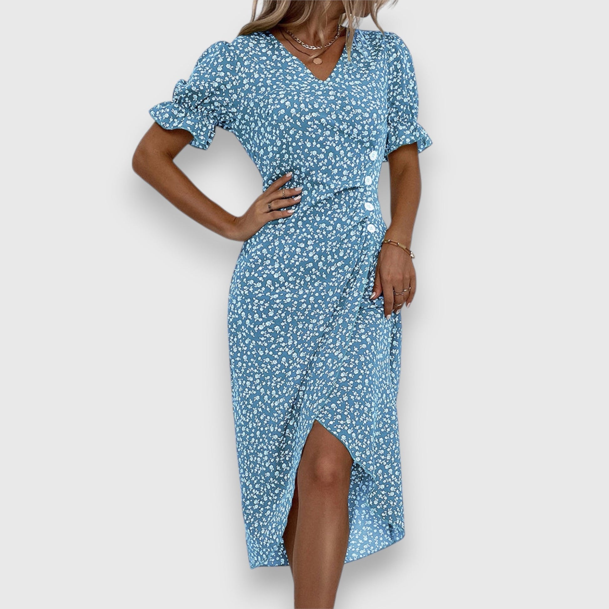 A woman wearing a light blue midi sundress with a white ditsy floral print, featuring puff sleeves, a V-neckline, and an asymmetrical wrap skirt with button details.