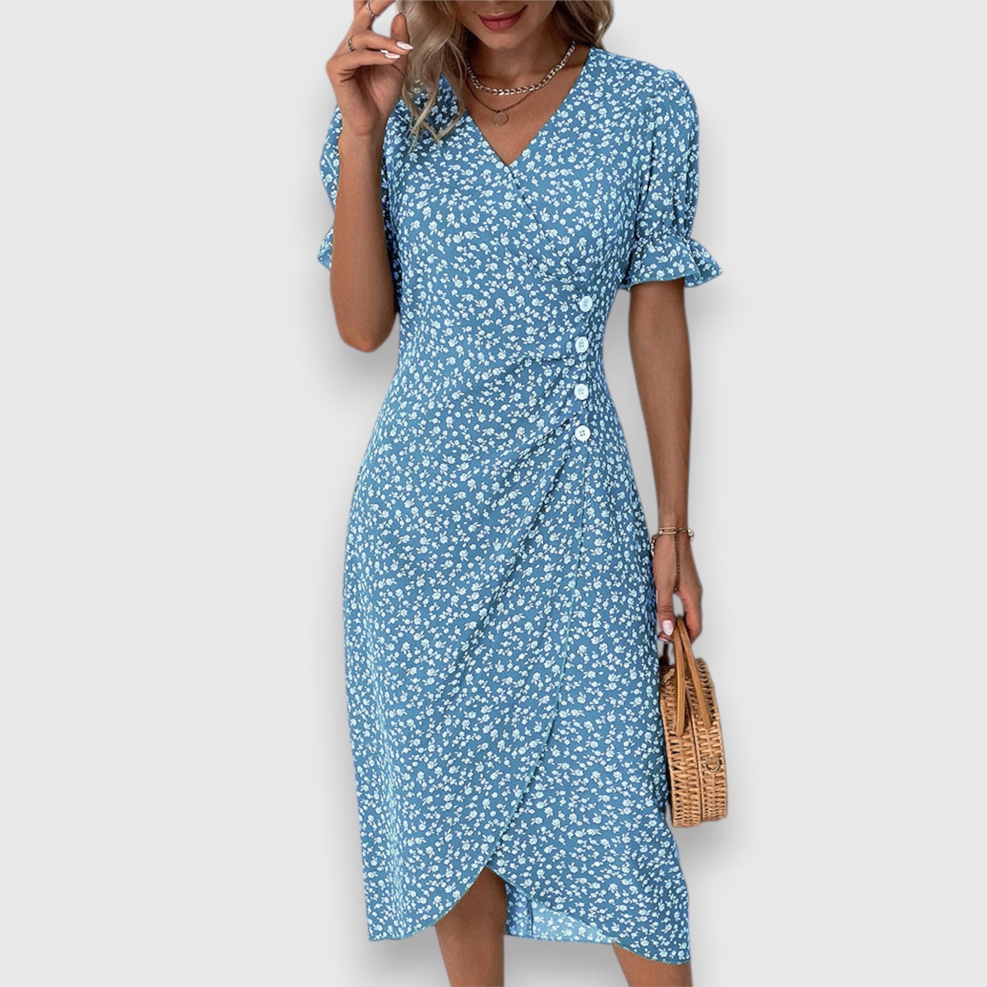 A woman wearing a light blue midi sundress with a white ditsy floral print, featuring puff sleeves, a V-neckline, and an asymmetrical wrap skirt with button details.