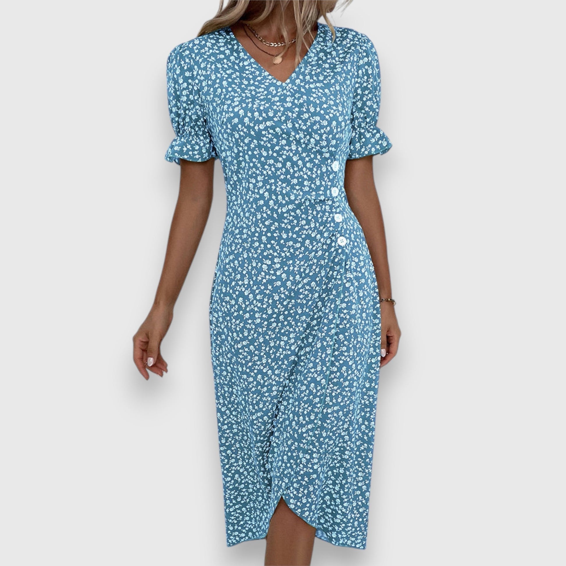 Blue - A woman wearing a light blue midi sundress with a white ditsy floral print, featuring puff sleeves, a V-neckline, and an asymmetrical wrap skirt with button details.