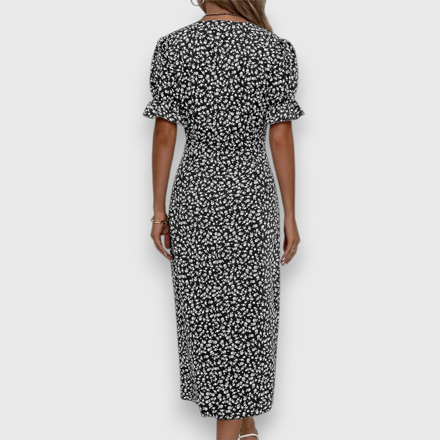 Black - A woman wearing a light blue midi sundress with a white ditsy floral print, featuring puff sleeves, a V-neckline, and an asymmetrical wrap skirt with button details.