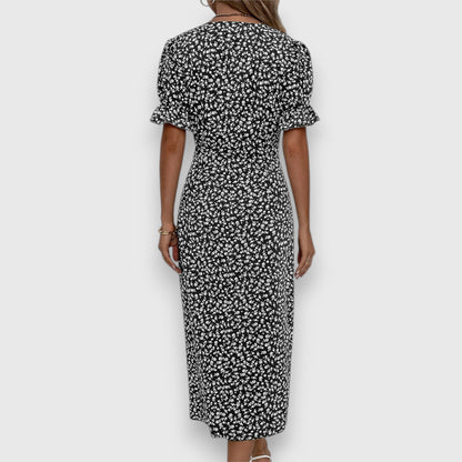 Black - A woman wearing a light blue midi sundress with a white ditsy floral print, featuring puff sleeves, a V-neckline, and an asymmetrical wrap skirt with button details.