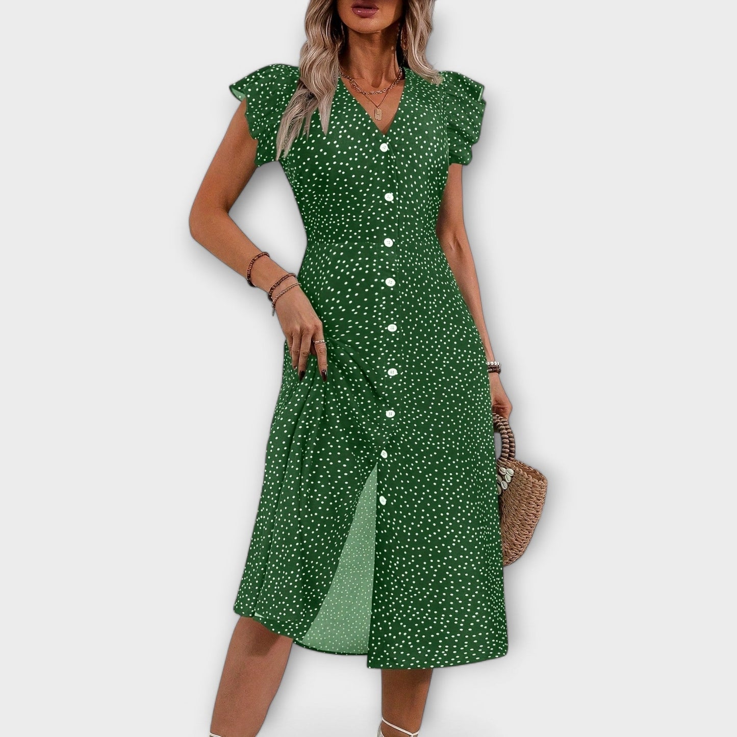 Model wearing a red and white ditsy polka dot midi sundress with a V-neckline, flutter sleeves, and button-down front, paired with a straw hat and white lace-up heels.