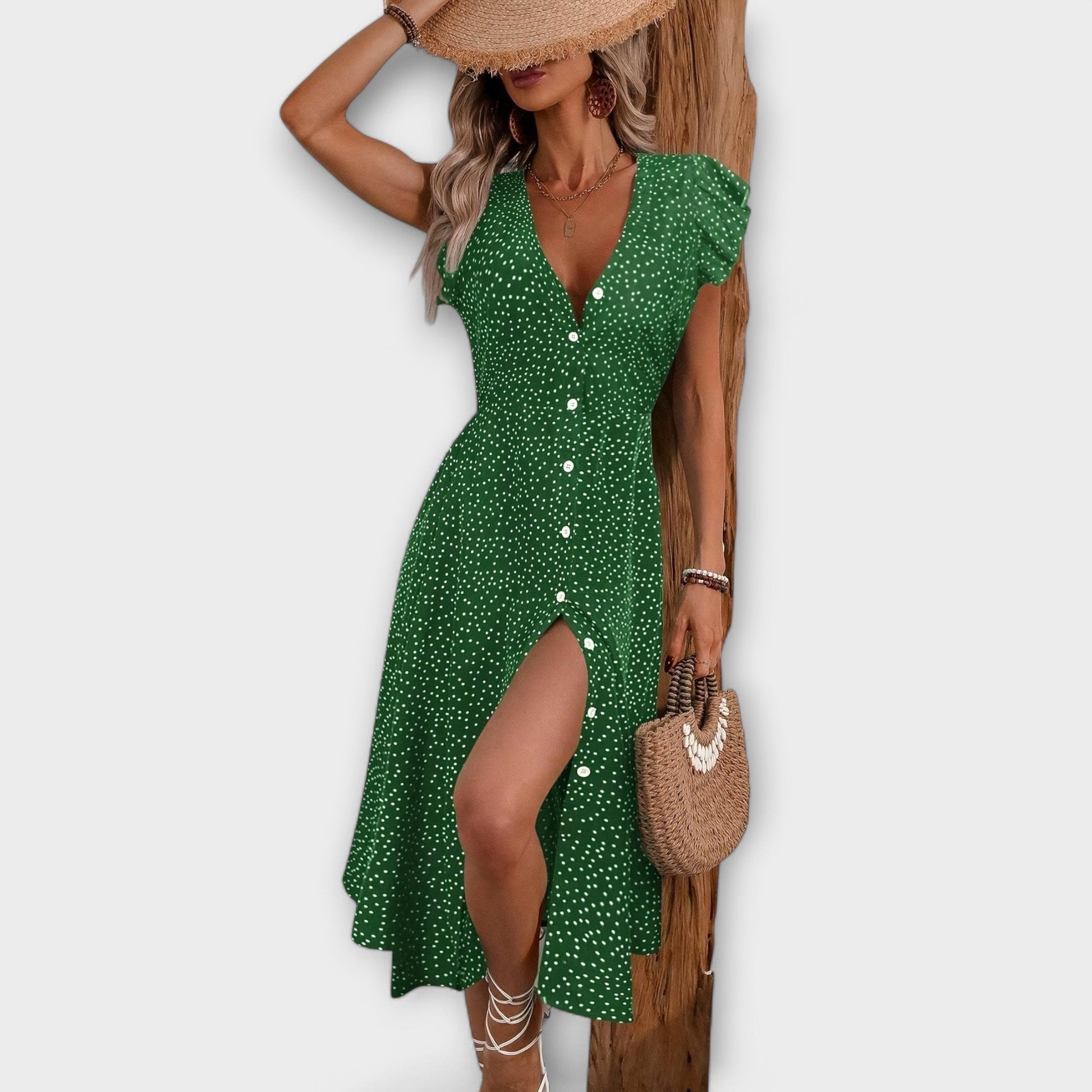 Model wearing a red and white ditsy polka dot midi sundress with a V-neckline, flutter sleeves, and button-down front, paired with a straw hat and white lace-up heels.