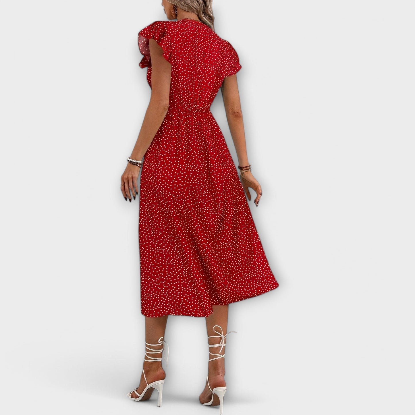 Model wearing a red and white ditsy polka dot midi sundress with a V-neckline, flutter sleeves, and button-down front, paired with a straw hat and white lace-up heels.
