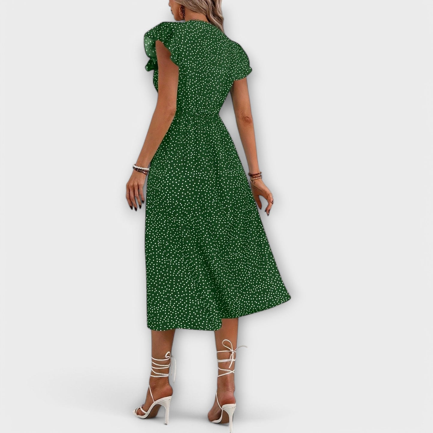 Model wearing a red and white ditsy polka dot midi sundress with a V-neckline, flutter sleeves, and button-down front, paired with a straw hat and white lace-up heels.