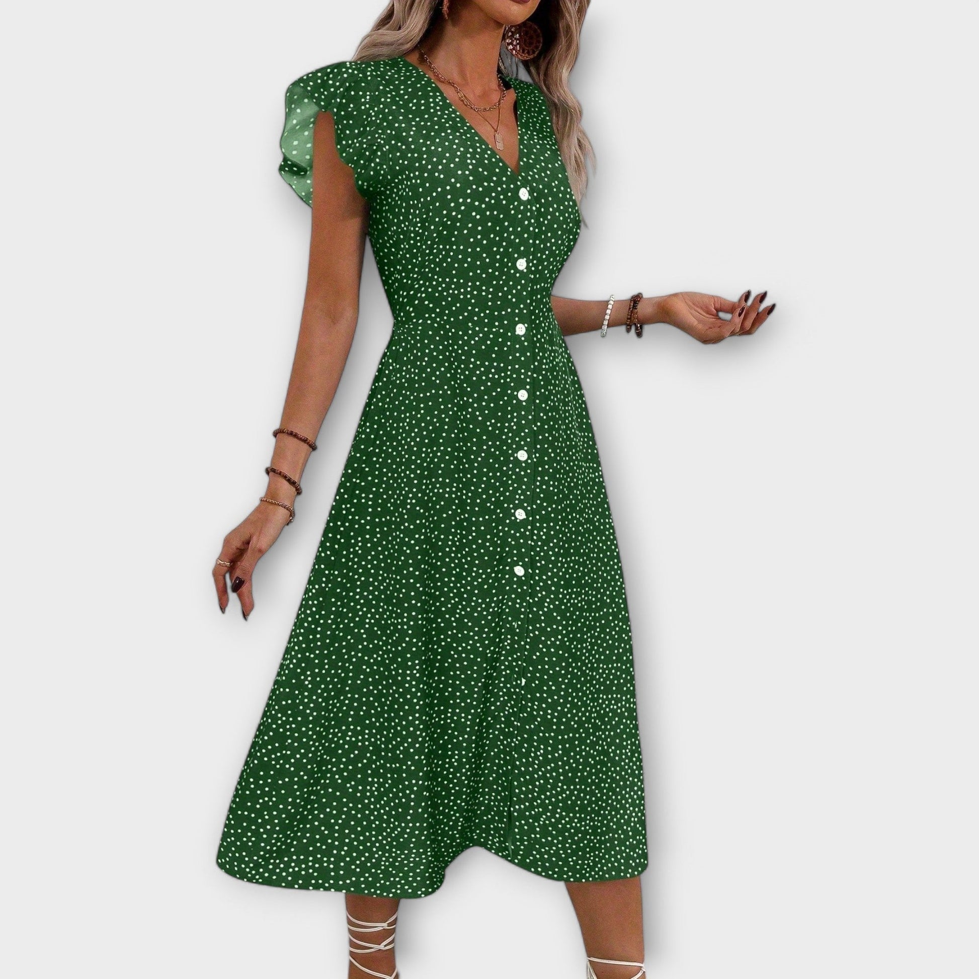 Model wearing a red and white ditsy polka dot midi sundress with a V-neckline, flutter sleeves, and button-down front, paired with a straw hat and white lace-up heels.