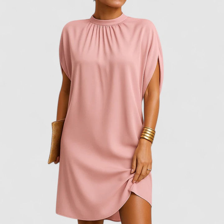 Pink - A woman wearing a dusty pink crepe shift dress featuring a gathered mock neckline, draped cap sleeves, and a relaxed silhouette.