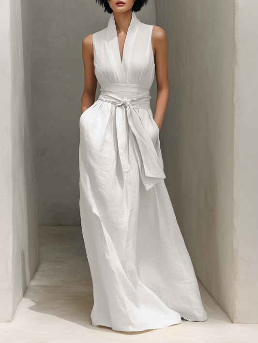 White - Model wearing a sleeveless V-neck maxi dress featuring a wide tie-waist and side pockets, standing in a minimalist architectural hallway.