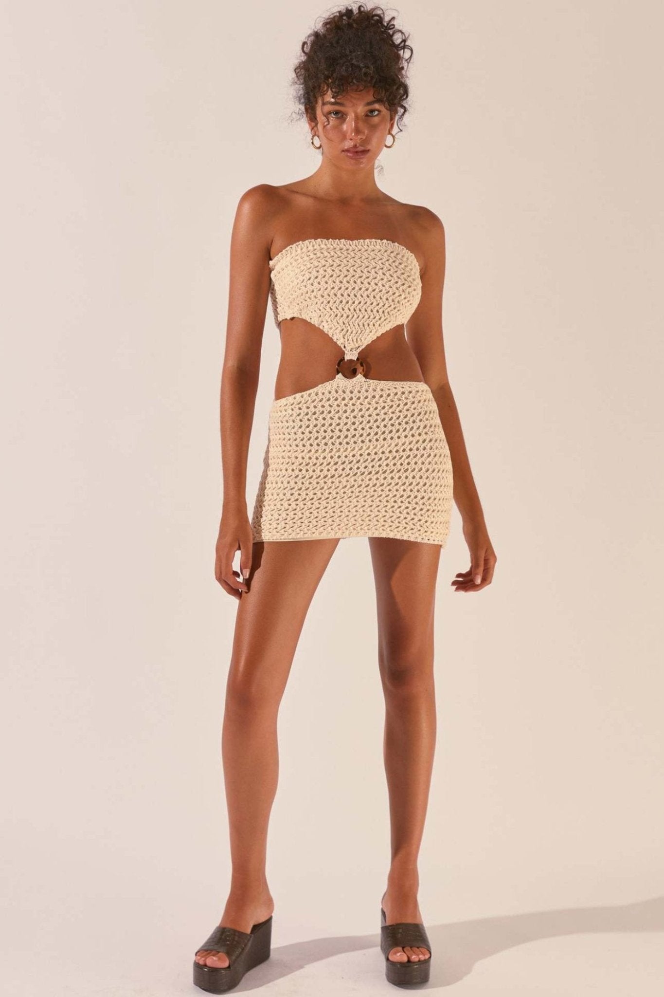 Woman wearing cream crocheted mini dress with cutout waist detail