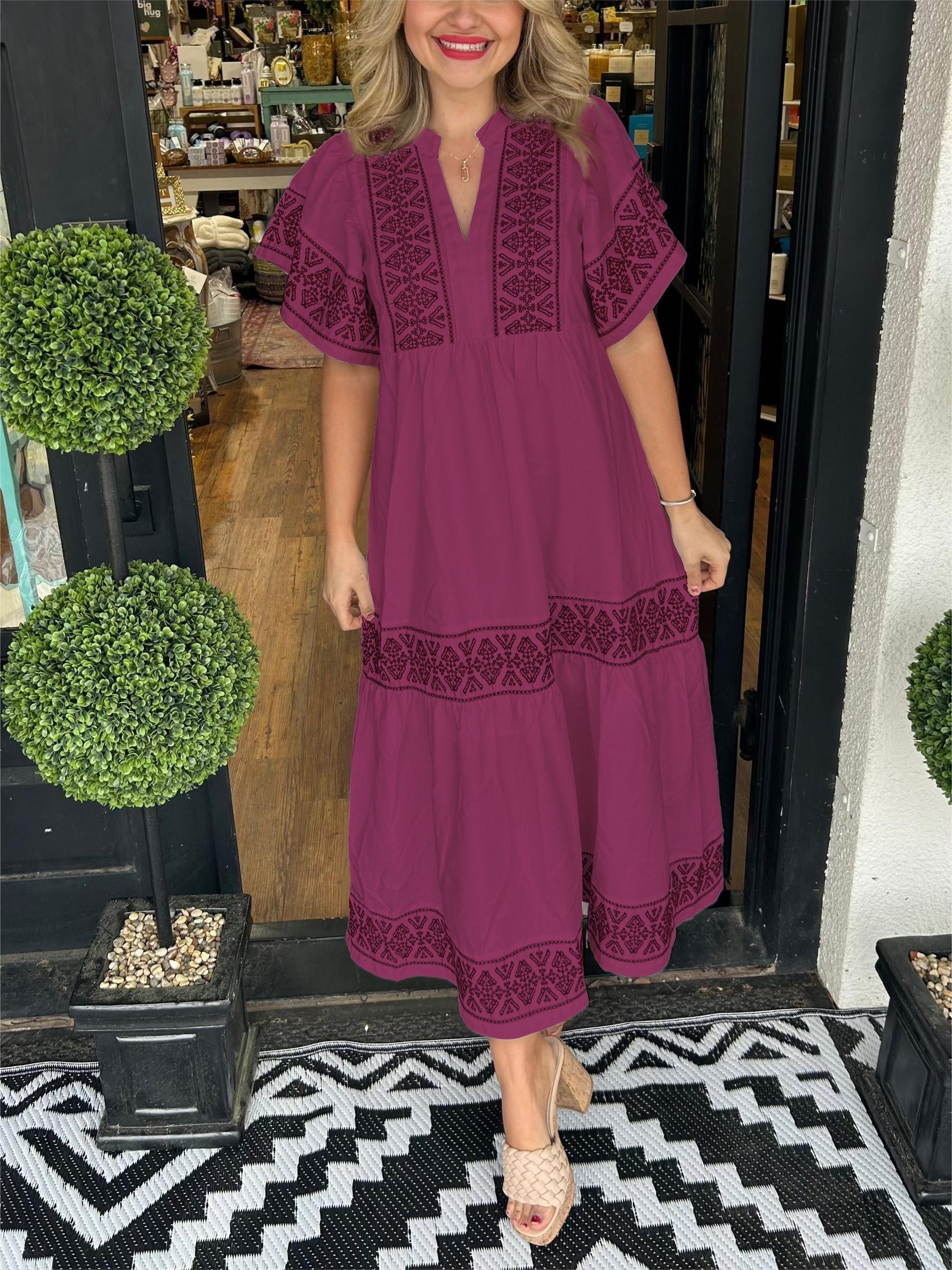 Wine Red - A woman wearing a black midi-length cotton dress featuring white geometric embroidery along the V-neckline, flutter sleeves, tiered skirt, and hem.