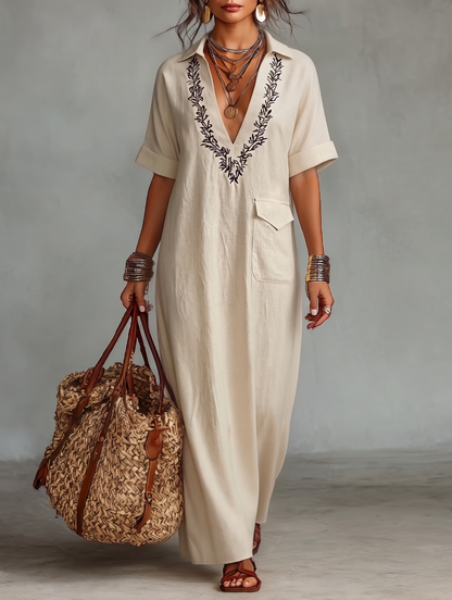 Beige - Model wearing a relaxed fit woven maxi dress with a collared V-neckline, intricate front embroidery, and a single patch pocket, styled with a woven tote bag.