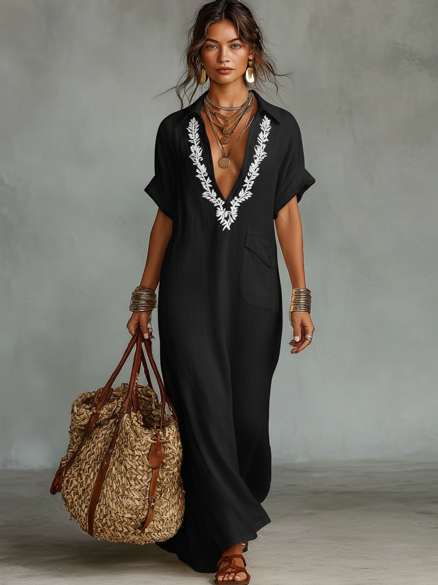 Black - Model wearing a relaxed fit woven maxi dress with a collared V-neckline, intricate front embroidery, and a single patch pocket, styled with a woven tote bag.
