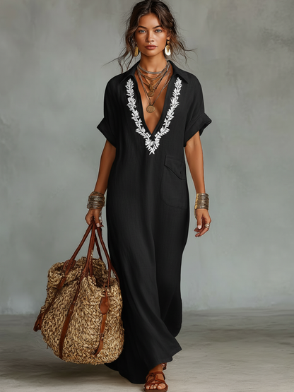 Black - Model wearing a relaxed fit woven maxi dress with a collared V-neckline, intricate front embroidery, and a single patch pocket, styled with a woven tote bag.