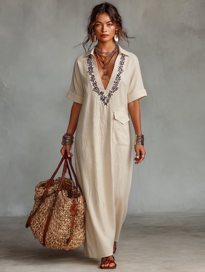 Black - Model wearing a relaxed fit woven maxi dress with a collared V-neckline, intricate front embroidery, and a single patch pocket, styled with a woven tote bag.