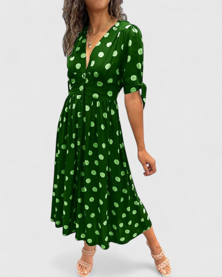 Green - A woman wearing an emerald green midi dress with a light green polka dot pattern, featuring a V-neckline, short sleeves with tie details, a button-front bodice, and a fluid A-line skirt.