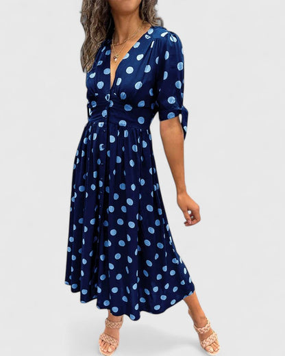 Blue - A woman wearing an emerald green midi dress with a light green polka dot pattern, featuring a V-neckline, short sleeves with tie details, a button-front bodice, and a fluid A-line skirt.