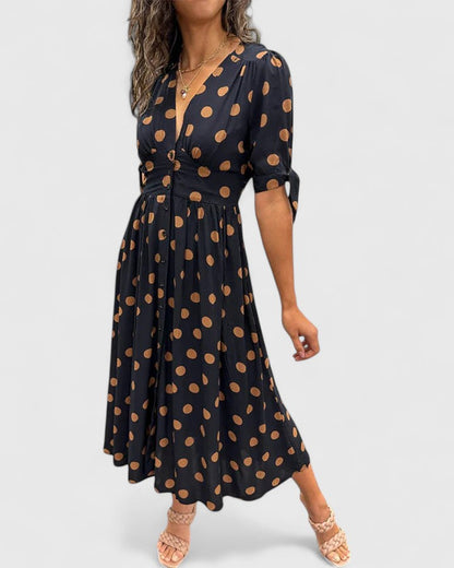 Black - A woman wearing an emerald green midi dress with a light green polka dot pattern, featuring a V-neckline, short sleeves with tie details, a button-front bodice, and a fluid A-line skirt.