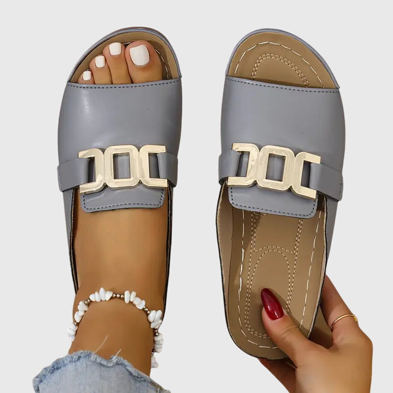 Gray - Pair of women's open-toe slide sandals featuring a smooth upper with prominent metallic link hardware across the vamp and a contoured stitched footbed.