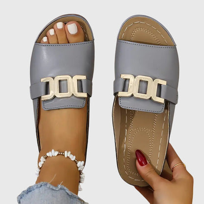 Gray - Pair of women's open-toe slide sandals featuring a smooth upper with prominent metallic link hardware across the vamp and a contoured stitched footbed.