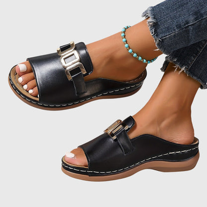 Black - Pair of women's open-toe slide sandals featuring a smooth upper with prominent metallic link hardware across the vamp and a contoured stitched footbed.