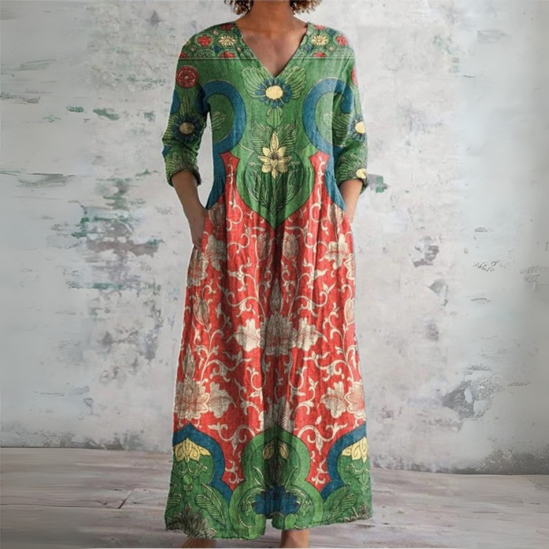3XL - Woman wearing a long, vibrant green and red maxi dress with a large floral and medallion print, featuring 3/4 sleeves and side pockets