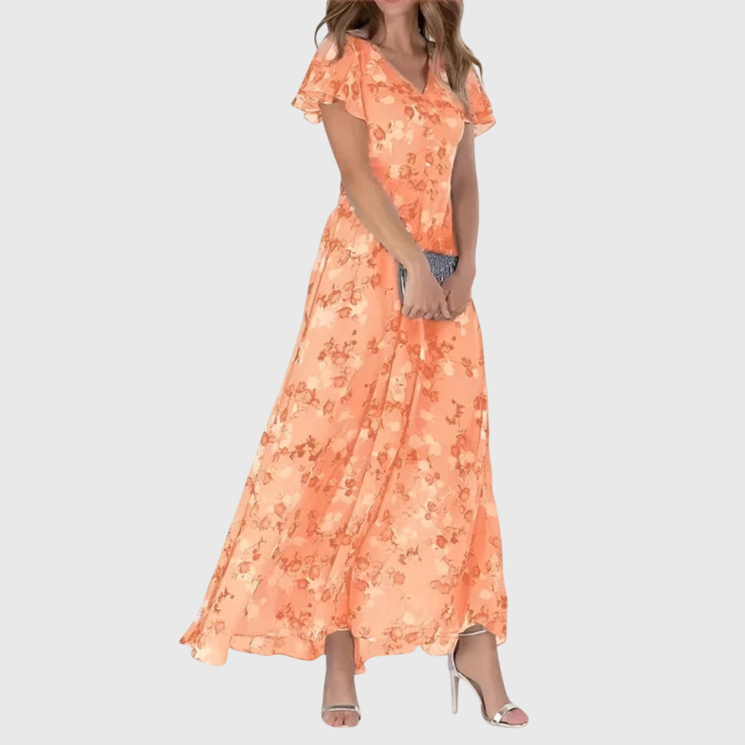 Orange - Woman wearing a peach watercolor floral chiffon maxi dress with flutter sleeves and a V-neckline, styled with metallic heels.