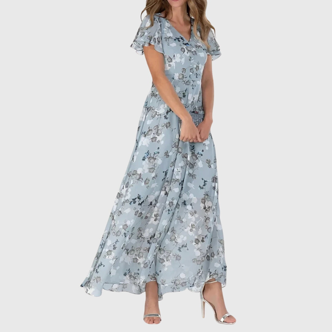 Blue - Woman wearing a peach watercolor floral chiffon maxi dress with flutter sleeves and a V-neckline, styled with metallic heels.