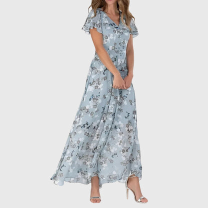 Blue - Woman wearing a peach watercolor floral chiffon maxi dress with flutter sleeves and a V-neckline, styled with metallic heels.