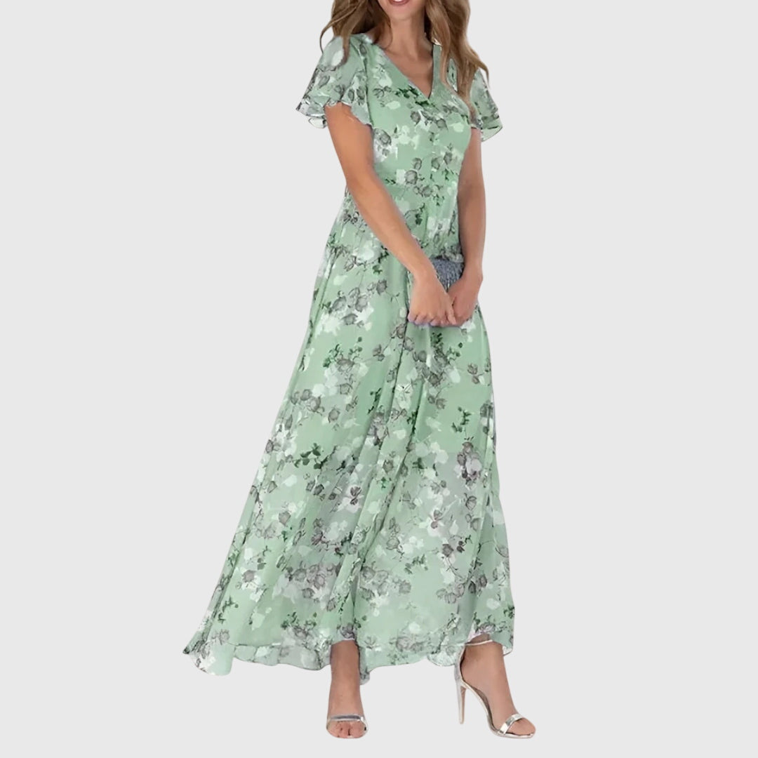 Green - Woman wearing a peach watercolor floral chiffon maxi dress with flutter sleeves and a V-neckline, styled with metallic heels.