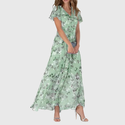 Green - Woman wearing a peach watercolor floral chiffon maxi dress with flutter sleeves and a V-neckline, styled with metallic heels.
