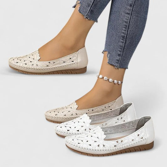 Women's slip-on loafers featuring a faux-leather upper with detailed floral cutouts, scalloped edges, and a textured flat sole.