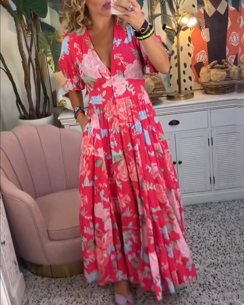 Red - Woman wearing a floral print maxi dress with short puff sleeves, a v-neckline, button front, and a tiered skirt, standing with one hand in her pocket