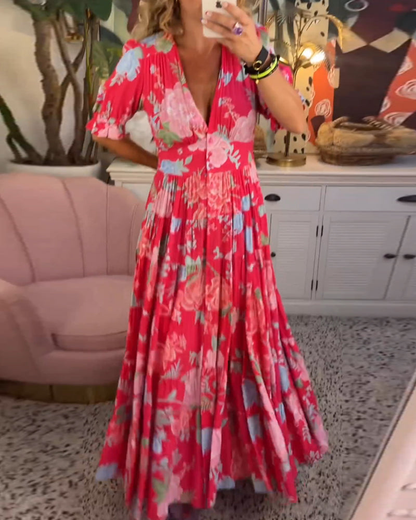 Red - Woman wearing a floral print maxi dress with short puff sleeves, a v-neckline, button front, and a tiered skirt, standing with one hand in her pocket