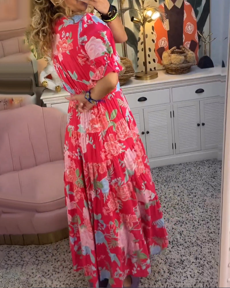 Red - Woman wearing a floral print maxi dress with short puff sleeves, a v-neckline, button front, and a tiered skirt, standing with one hand in her pocket