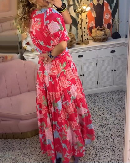 Red - Woman wearing a floral print maxi dress with short puff sleeves, a v-neckline, button front, and a tiered skirt, standing with one hand in her pocket