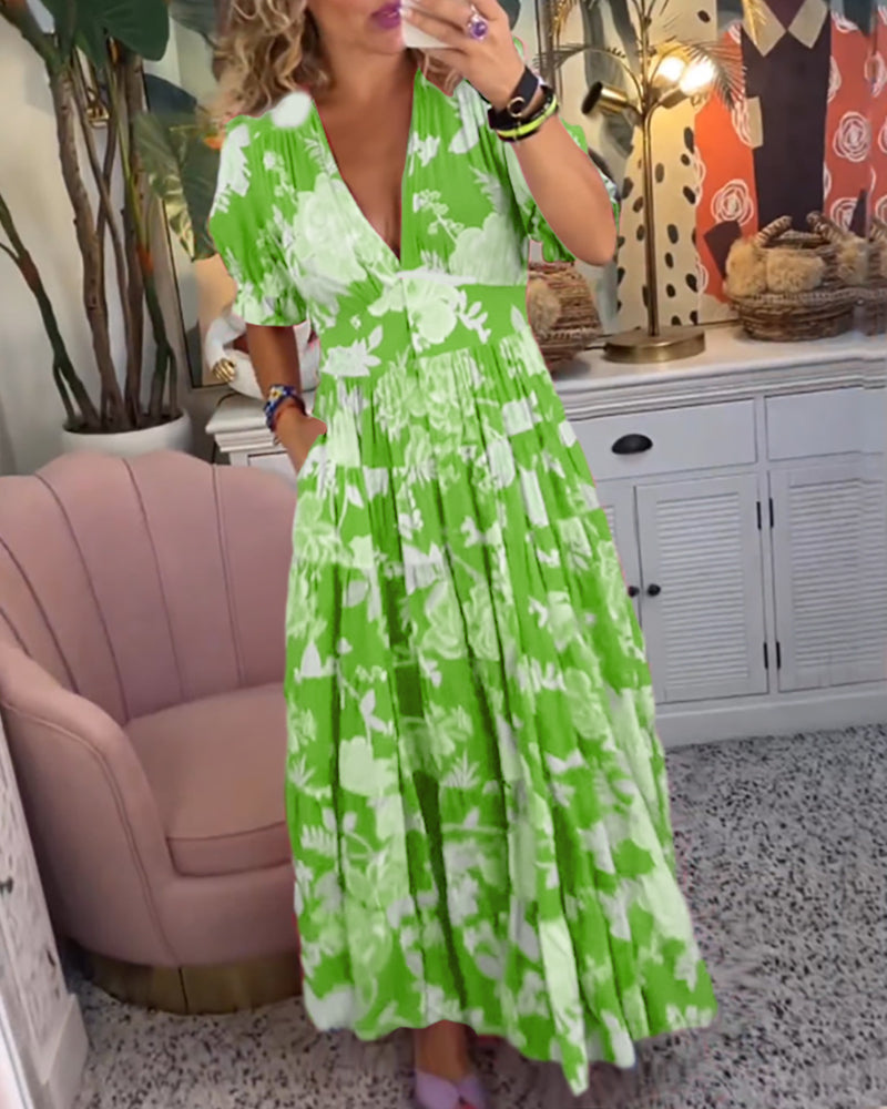 Light Green - Woman wearing a floral print maxi dress with short puff sleeves, a v-neckline, button front, and a tiered skirt, standing with one hand in her pocket