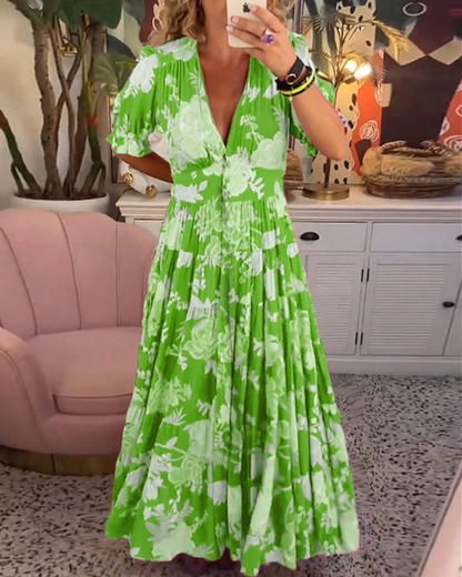 Light Green - Woman wearing a floral print maxi dress with short puff sleeves, a v-neckline, button front, and a tiered skirt, standing with one hand in her pocket