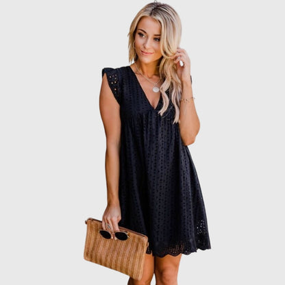 Black - A woman wearing a black V-neck cotton eyelet mini sundress with flutter sleeves and a scalloped hem, holding a straw clutch.