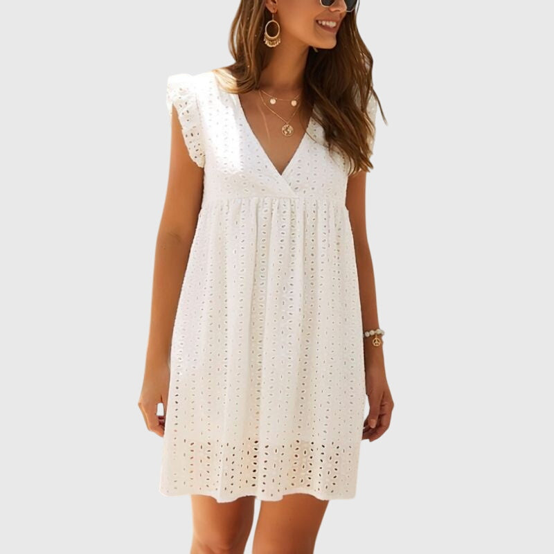 White - A woman wearing a black V-neck cotton eyelet mini sundress with flutter sleeves and a scalloped hem, holding a straw clutch.