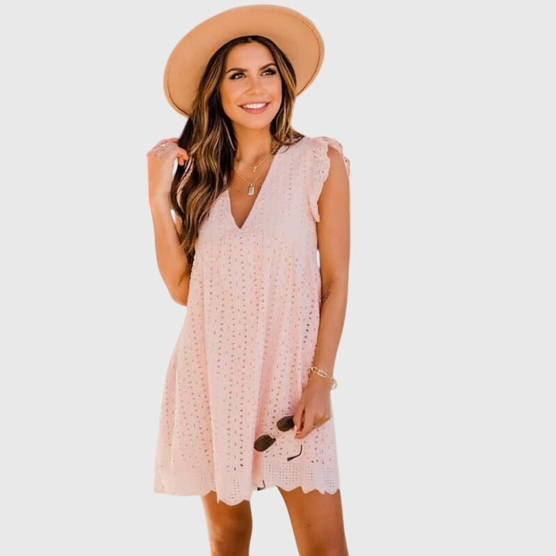 Pink - A woman wearing a black V-neck cotton eyelet mini sundress with flutter sleeves and a scalloped hem, holding a straw clutch.