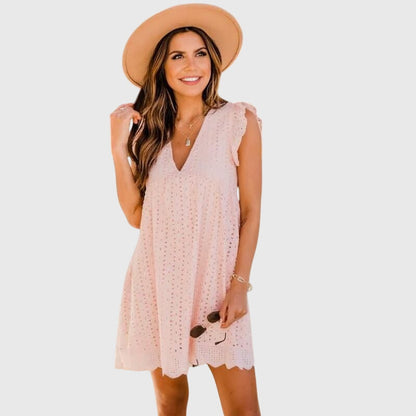 Pink - A woman wearing a black V-neck cotton eyelet mini sundress with flutter sleeves and a scalloped hem, holding a straw clutch.