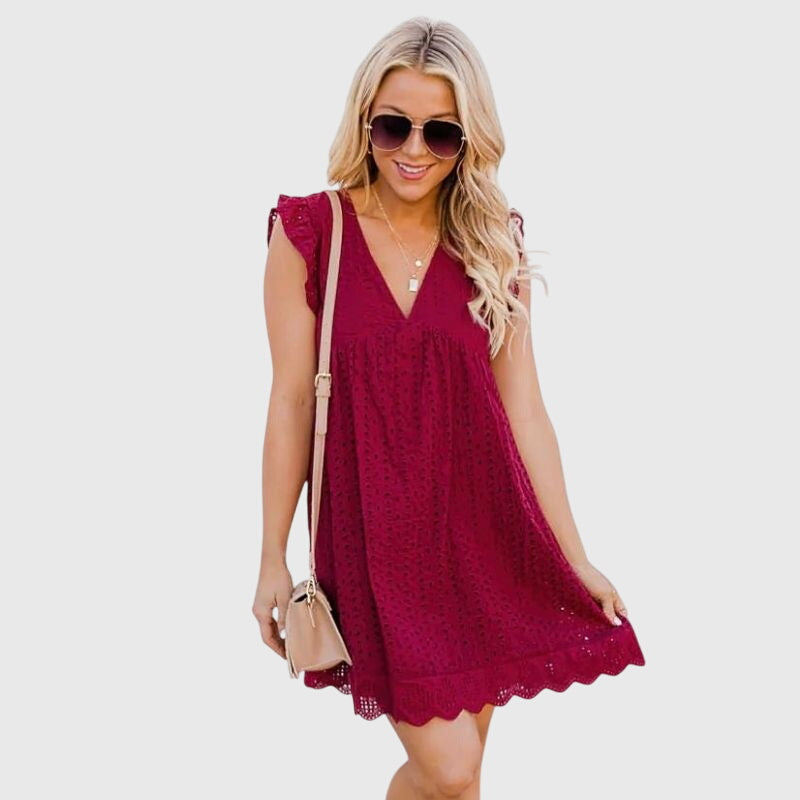 Red - A woman wearing a black V-neck cotton eyelet mini sundress with flutter sleeves and a scalloped hem, holding a straw clutch.