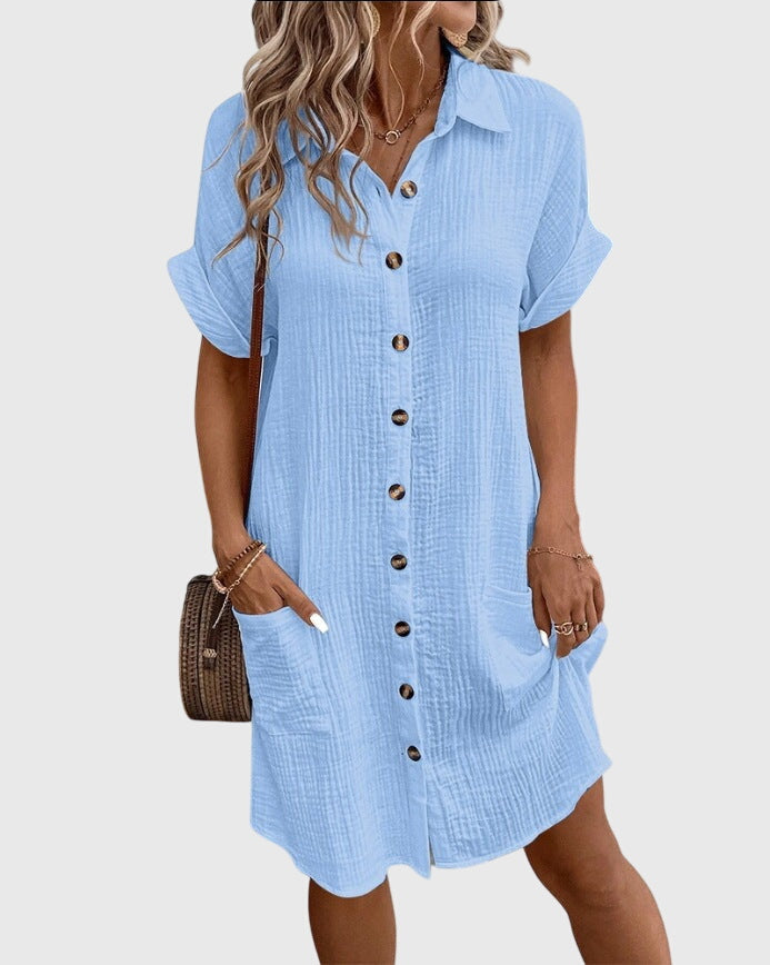 Light Blue - A woman wearing a white, short-sleeved cotton gauze button-down shirt dress with front patch pockets and a pointed collar.