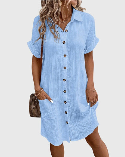 Light Blue - A woman wearing a white, short-sleeved cotton gauze button-down shirt dress with front patch pockets and a pointed collar.