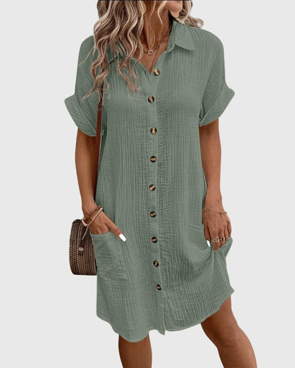 Olive Green - A woman wearing a white, short-sleeved cotton gauze button-down shirt dress with front patch pockets and a pointed collar.