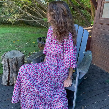 Purple - Woman wearing a long sleeve geometric print tiered maxi dress with puff sleeves walking on a sidewalk