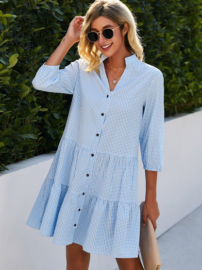 Light Blue - Woman wearing a gingham poplin mini dress with 3/4 sleeves, a button front, and a tiered skirt, standing outdoors.